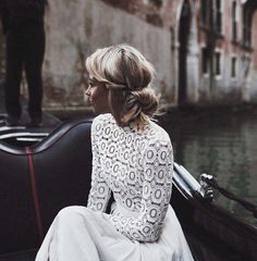 a woman sitting in a gondola on the side of a river wearing a white dress