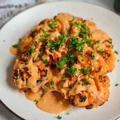 a white plate topped with cauliflower covered in gravy and garnished with parsley