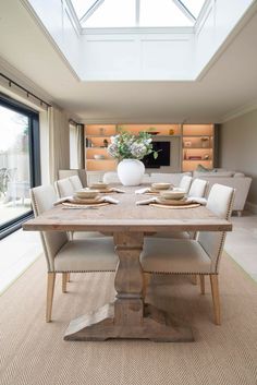 a dining room table with white chairs and a vase on top of it in front of a large window