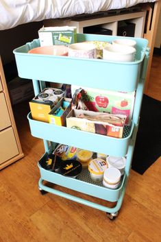 a blue cart filled with lots of items on top of a wooden floor next to a bed