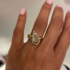 a woman's hand with a yellow gold ring and a pear shaped diamond on it