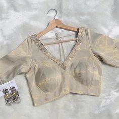 Elevate your traditional wardrobe with this stunning light beige golden sequin blouse, designed for elegance and comfort. Crafted from luxurious sequin fabric, this blouse features a stylish V-neck on both the front and back, perfect for adding a touch of sophistication to your ensemble. The back thread detailing adds a unique flair, while the lace trim around the neckline enhances its delicate beauty. Ideal for pairing with sarees or lehengas, this versatile piece will make you stand out at wed Cheap Gold Blouse With Cutdana, Elegant Beige Traditional Wear For Navratri, Elegant Lehenga With Zari Work And V-neck, Elegant V-neck Blouse For Festive Occasions, Elegant Festive V-neck Blouse, Elegant V-neck Lehenga With Unstitched Blouse, Wedding Lehenga With Unstitched Blouse And V-neck, Elegant V-neck Tops With Zari Work, Elegant V-neck Top With Zari Work