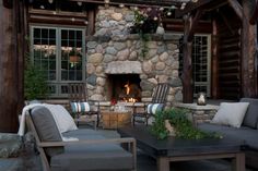 an outdoor fireplace with chairs and tables in front of the fire place at night time