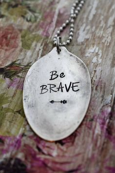 a silver necklace with the words be brave written on it and an arrow in black ink