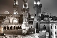 black and white photograph of an old city at night with the moon in the sky