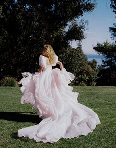 a woman in a white dress is walking through the grass