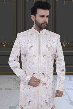 Introducing the V20-S45 Mens Sherwani, adorned with intricate peacock and elephant embroidery. This stunning white sherwani is accented with rich red details. Perfect for grooms seeking luxurious elegance on their special day. Elevate your style with this exclusive piece. Elegant Nehru Jacket For Traditional Ceremonies, White Nehru Jacket With Naqshi For Transitional Season, Elegant Nehru Jacket For Diwali Ceremonies, Ceremonial White Traditional Wear With Naqshi, Ceremonial White Naqshi Traditional Wear, White Naqshi Traditional Wear For Ceremonial Occasions, White Nehru Jacket For Wedding And Transitional Season, Elegant Sherwani For Traditional Ceremonies, White Bandhgala With Dabka Work For Traditional Ceremonies