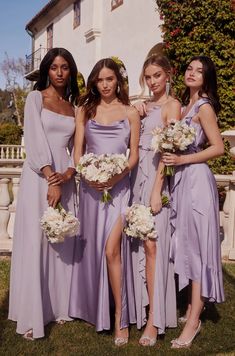 four bridesmaids in lavender dresses posing for a photo outside the house with their bouquets