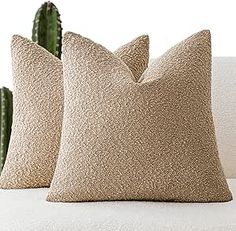 two beige pillows sitting on top of a white couch next to a green cactus plant