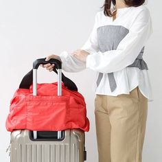 A woman standing with a grey suitcase with a large red bag through the handle she holds. Functional Foldable Travel Accessories For On-the-go, Versatile Travel Bag With Zipper Pocket For Overnight Trips, Versatile Travel Bag With Zipper For Overnight Trips, Travel Bag With Zipper Pocket For Overnight Trips, Practical Travel Bag For Weekend Trips, Practical Large Capacity Travel Bag For On-the-go, Practical Travel Bag With Zipper Pocket For Weekend Trips, Foldable Functional Travel Accessories, Versatile Packable Bag For Trips