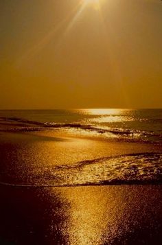 the sun shines brightly over the ocean on a beach with waves coming in to shore