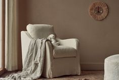 a chair with a blanket on it in front of a window and a wall clock