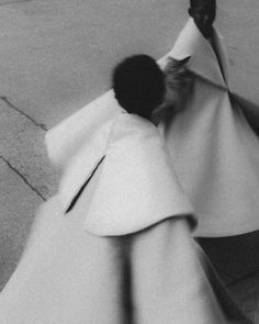 a black and white photo of a woman walking down the street wearing a long coat