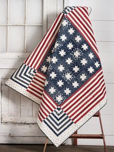 an american flag quilt is displayed on a stand in front of a white painted wall