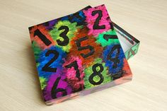 a colorful box with numbers painted on it sitting on a table next to a pair of scissors