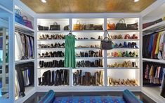 a closet filled with lots of different types of shoes and handbags on shelves next to a blue couch