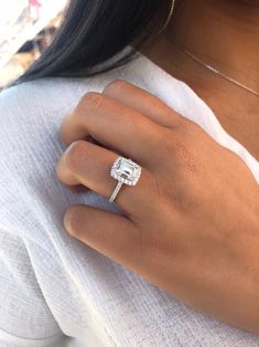 a woman's hand with a diamond ring on her left hand and a white top