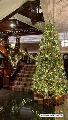 a decorated christmas tree sitting in the middle of a lobby next to a stair case