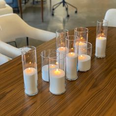 candles are lined up on a table with chairs in the background