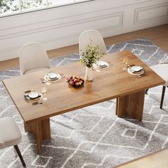 a wooden table with white chairs and plates on it in front of a large window