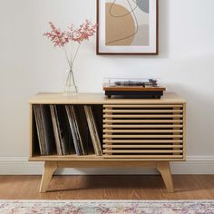 a record player on top of a wooden cabinet next to a vase with flowers in it