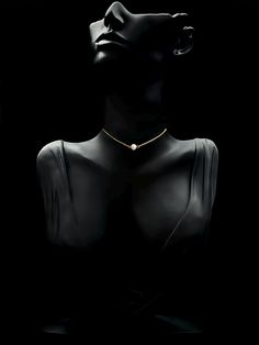 a black mannequin with a gold necklace on it's neck, in the dark