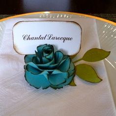 a white plate with a blue rose on it and a name tag in the center