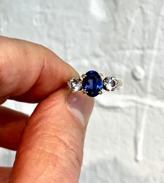 Lab grown sapphire and white spinel 9ct solid gold trilogy ring. This blue stone does test as sapphire, but I think it's more likely to be lab grown, but looks absolutely amazing. CONGRATS: Excellent  CENTRE STONE SIZE: 8mm x 6mm ( 1.8 carat ) CURRENT FINGER SIZE: UK size L. Can be altered to the sizes on the drop down menu. WEIGHT: 2.7g This ring has been professionally checked, cleaned and polished. Comes in a new box. Three Stone Sapphire Round Ring Fine Jewelry, Fine Jewelry Sapphire Three Stone, Timeless Round Three Stone Sapphire Ring, Heirloom Three Stone Sapphire Ring, Heirloom Sapphire Ring With Three Stones, Heirloom Sapphire Three Stone Ring, Fine Jewelry Three-stone Sapphire Ring, Timeless Sapphire-colored Cubic Zirconia Ring, Timeless Cubic Zirconia Ring In Sapphire Color