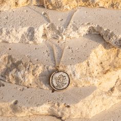 a necklace with an image of a flower on it sitting in the sand next to some rocks