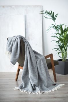 a grey blanket sitting on top of a wooden chair next to a potted plant