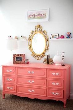 a pink dresser with a gold mirror above it and pictures on the wall behind it