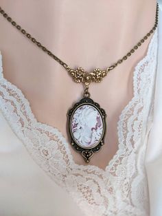 This beautiful vintage-style Cameo necklace features a classic portrait cameo of a Greek Goddess. The cameo has a chalk-white relief on a faded-ruby background. Set in an ornate antique brass pendant that is suspended from a beautiful vintage style floral necklace connector.  A quintessential gift for anyone who loves vintage-inspired Victorian and Gothic jewelry.  Size: The ornate necklace pendant is silver-plated brass and measures 40 mm (1 1/2 inches) long, and 24 mm (just under 1 inch) wide. Classic Cameo Necklace As Gift, Classic Cameo Necklace For Gift, Elegant Cameo Necklaces For Wedding, Elegant Cameo Necklace For Wedding, Vintage Cameo Jewelry For Wedding, Ornate Cameo Jewelry For Vintage Events, Antique Gold Cameo Necklace For Wedding, Cameo Pendant Necklace For Wedding, Elegant Cameo Necklace For Vintage Events