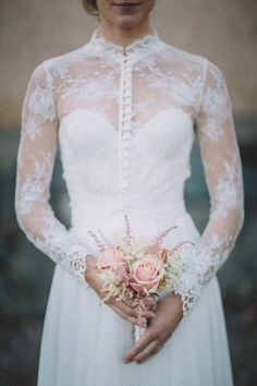 a woman in a white dress holding a bouquet and wearing a long sleeved lace top