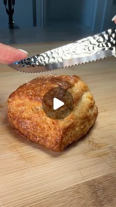 a person holding a knife over a piece of bread on top of a wooden table