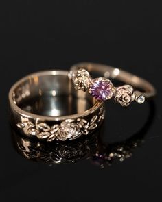 two gold wedding rings with pink and white diamonds on black background, close - up