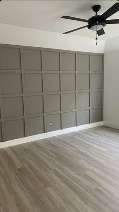 an empty room with wood flooring and ceiling fan in the corner, painted gray