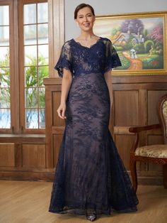 a woman in a blue dress standing on a wooden floor next to a chair and window