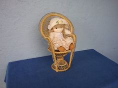 a teddy bear sitting in a wicker chair on a blue tableclothed surface