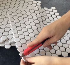 a person holding a red toothbrush over a white hexagonal tile