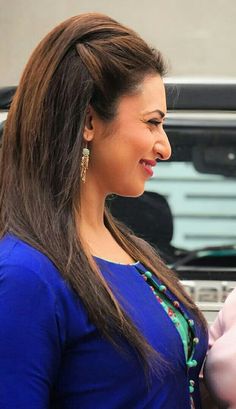 a woman with long brown hair wearing a blue shirt and pink pants standing in front of a car