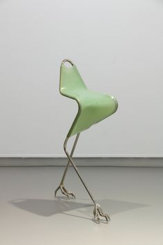 a green chair sitting on top of a metal stand in front of a white wall