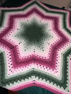 a crocheted blanket is laying on top of a bed with green and pink sheets