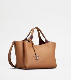 Bag in soft exposed grain leather, with Tod's logo stamped on the front, flat handles and removable shoulder strap. The interior comes with three compartments separated by zipped central pockets. An elegant creation enhanced by distinctive iconic detailing, such as the metal T Timeless pendant and T-stitching. Tods Bag, Micro Bags, Micro Bag, Leather Stamps, Brown Leather Bag, Timeless Accessories, Brown Bags, Timeless Handbag, Leather Items