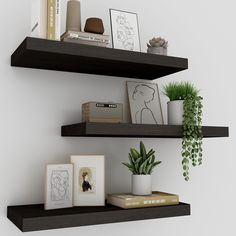 two black floating shelves with pictures, plants and other items on them in front of a white wall