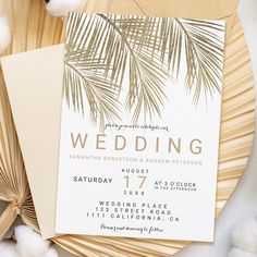 a wedding card with palm leaves on it and cotton floss around the edges, in front of a fan