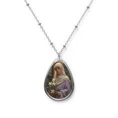 "Pendant height - 1.50\" Pendant width - 1.00\" Chain length - 20.47\" .: Zinc alloy pendant and necklace chain .: Ellipse-shaped pendant .: White aluminum print surface Saint Adele, the daughter of King Dagobert II of Germany, graced the pages of history with her remarkable life marked by faith, virtue, and regal devotion. Born in the 7th century into the royal lineage, Adele's story unfolds as a tapestry woven with threads of piety and noble responsibility. Despite her royal status, Adele chos Royal Status, Christian Virtues, Daughter Of King, Royal Lineage, Tapestry Woven, Spiritual Values, Necklace Art, Spiritual Beliefs, Oval Necklace