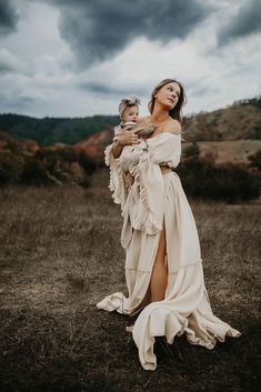 a woman holding a baby in her arms while standing on top of a dry grass field