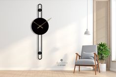 a black clock hanging on the wall next to a chair in a room with white walls