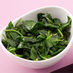 a white bowl filled with spinach on top of a pink table