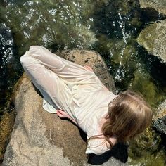 a woman laying on top of a rock next to water